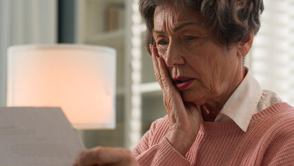 Close up old 60s Caucasian woman retired lady 70s senior female granny reading bad news open paper envelop read letter sad upset shocked unpleasant notification high taxes financial health problems