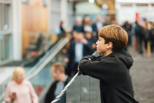 Boy standing in airport terminal looking out window at planes outside