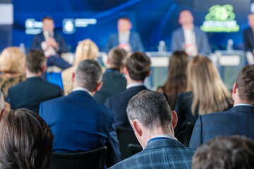 Fototapeta premium Business professionals attending a conference with a panel of speakers on stage discussing various topics.