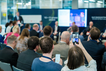 Business professionals attend a conference, engaging with the speaker and capturing moments on...