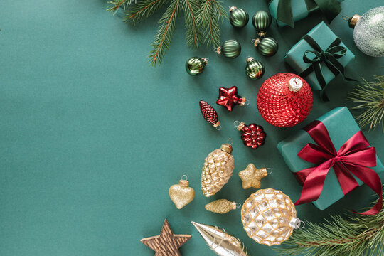 Overhead view of assorted Christmas baubles, ornaments, wrapped gift boxes and fir branches on a green background