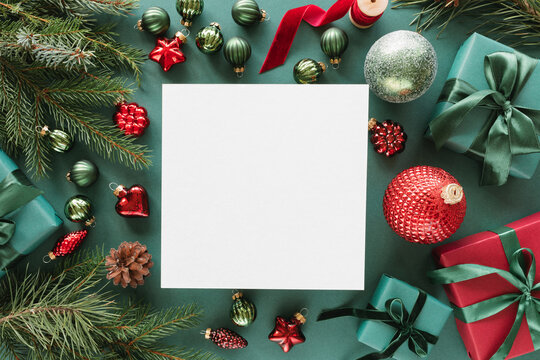 Overhead view of a blank piece of paper surrounded by wrapped Christmas gifts, fir branches, Christmas baubles, ornaments, pinecones and ribbon