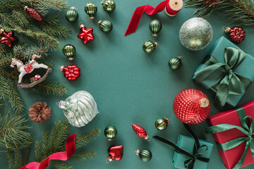 Overhead view of wrapped Christmas gifts, fir branches, Christmas baubles, ornaments, pinecones and ribbon on a green background