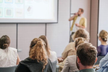 Speaker engaging audience at business seminar, presenting information on screen in formal...