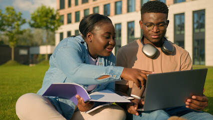 Two African American friends students high school pupils classmates university college academy in park outdoors learning studying together laptop computer online e-learning laughing drinking coffee