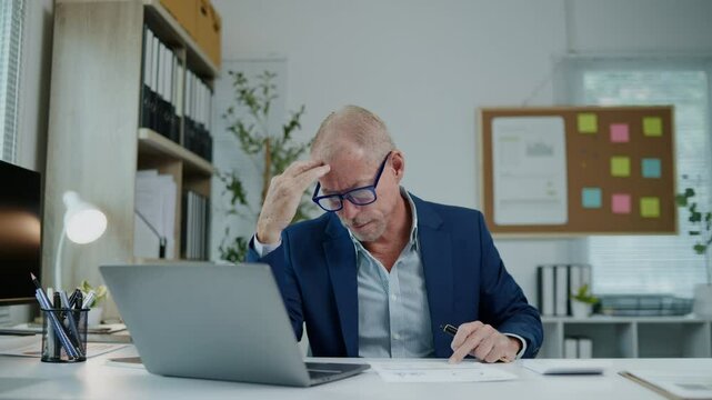 Businessman is seriously stressed and angry working on laptop and document paperwork and headache due to office syndrome on laptop and paperwork in the office.