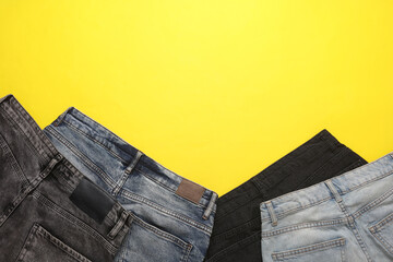 Assortment of different jeans on a yellow background. Top view. Copy space