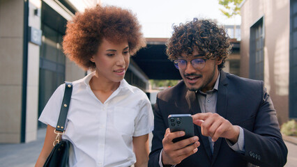 Two diverse multiracial business people in city together multiethnic partners colleagues African American woman Indian Arabian man friends win mobile phone success achieve scream celebrate victory