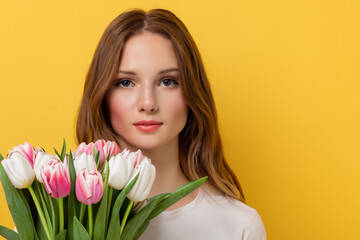 Fototapeta premium Girl in yellow with tulips on the . woman flower spring concept. girl is arranging bouquet of tulips in yellow on a . a girl in yellow with a bouquet of tulips on lifestyle a.