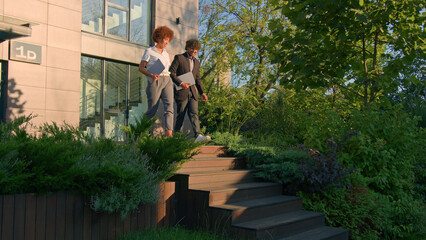 Two diverse multiracial business people partners colleagues African woman Indian Arabian man businesswoman and businessman talking friendly smiling happy conversation leaving office in city walk go