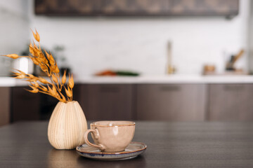 Coffee cup and vase with dry plants at wooden kitchen table