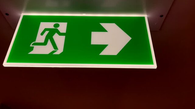 an illuminated emergency exit sign with a green background, featuring a person running towards the right arrow, Ideal for safety, emergency preparedness, architectural content