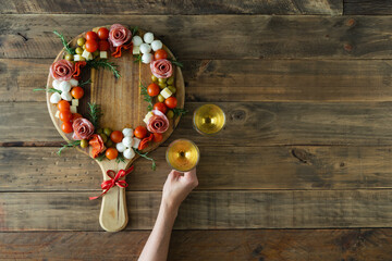 Hand holding a glass of wine. The food is arranged in the shape of a crown, there are other pieces of cheese, salami and vegetables on the table.