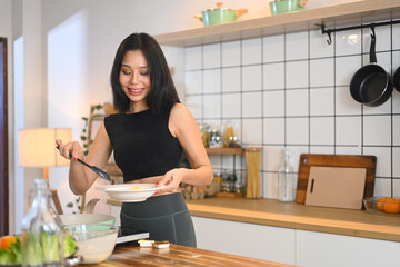 Beautiful young woman in activewear preparing a nutritious breakfast or snack at kitchen counter