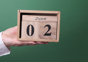 Hand holding a wooden block calendar with the date June 2 on green background