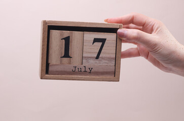 Female Hand holding wooden block calendar with the date July 17 on beige background