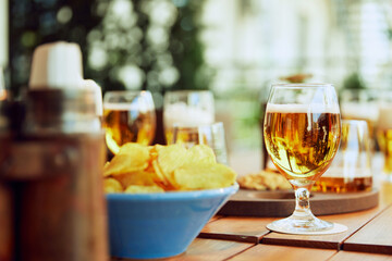 Glasses of beer and bowl of potato chips on wooden table at outdoor cafe during warm sunny day. Concept of party, celebration, leisure time, Oktoberfest