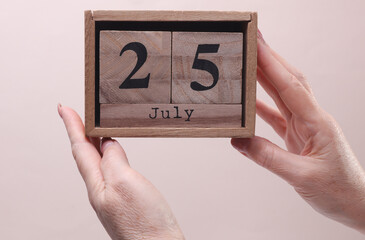 Female Hand holding wooden block calendar with the date July 25 on beige background