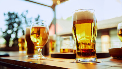 Glasses of lager golden beer with thick foamy head standing on a wooden table at cafe. Outdoor places with beautiful view. Concept of party, celebration, leisure time, Oktoberfest