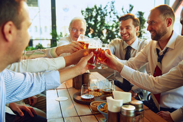 Group of cheerful men, business people meeting at outdoor cafe, clinking glasses with lager beer and celebrating successful deal. Concept of business, meeting, celebration, leisure time, Oktoberfest