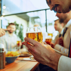 Focus on male hand holding lager beer. Business people, colleagues meeting at local bar, drinking beer, talking and celebrating successful collaboration. Concept of business, meeting, fun, Oktoberfest