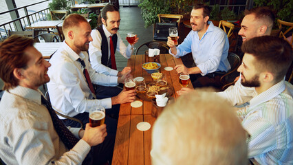 Colleagues, businessmen relaxing at the bar with beers, balancing work with bit of fun. Celebrating well-coordinated teamwork and success. Concept of business, meeting, fun, Oktoberfest