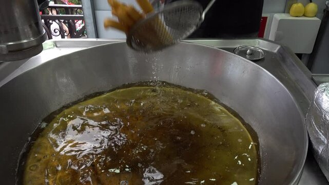 A street food vendor fries churros in a bustling outdoor setting, capturing the sizzling action and the golden treats as they cook in hot oil.
