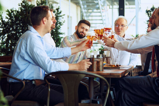 Group of positive men, business people, colleagues and partners meeting in informal settings, at bar to drink beer and lead discussing over projects. Concept of business, meeting, fun, Oktoberfest - Powered by Adobe