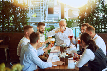 Productive meeting, businessmen in formal wear gathering at outdoor bar, drinking beer, talking, laughing and relaxing after hard working week. Concept of business, meeting, leisure time, Oktoberfest