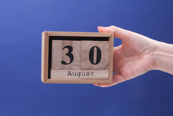 Female Hand holding wooden block calendar with the date August 30 on a blue background