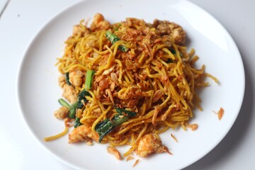 Delicious fried yellow noodles on a white plate close up view.