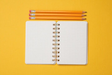Notepad with pencils on a yellow background. Top view