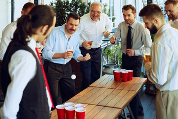 Businessmen, colleagues taking break, playing beer pong at the bar, mixing work with playful and joyful time. Concept of business, meeting, fun, celebration, leisure time, Oktoberfest