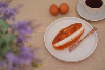 Eclair on a white plate with wooden table, top view.