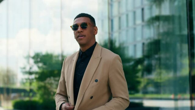Smiling stylish fashionable confident African American business man walking in city outdoors wearing black sunglasses businessman guy male entrepreneur smile at camera take off eyewear style fashion