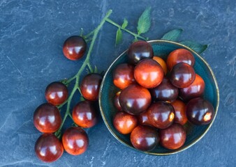 Black tomatoes of Indigo Rose in a bowl on the stone table. This natural form is rich in anthocyanin in black peel and good for our health.