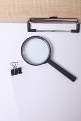 White blank sheet of paper with Black binder and magnifying glass on the table