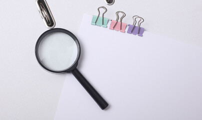 White blank sheet of paper with colored binders and magnifying glass