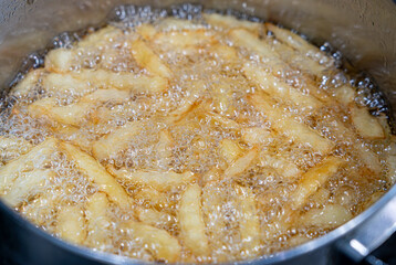 Potatoes in boiling oil, homemade french fries, deep fried potato cooking in metal fryer pot, fat fast food