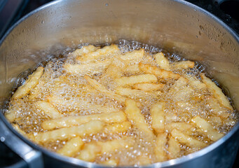 Potatoes in boiling oil, homemade french fries, deep fried potato cooking in metal fryer pot, fat fast food