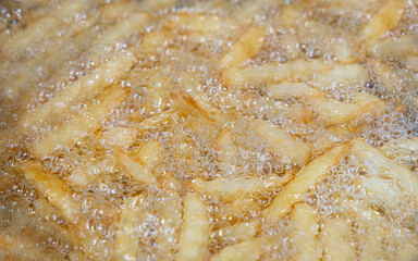 Potatoes in boiling oil, homemade french fries, deep fried potato cooking in metal fryer pot, fat fast food