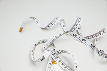 White measuring tape coiled loosely on a plain background