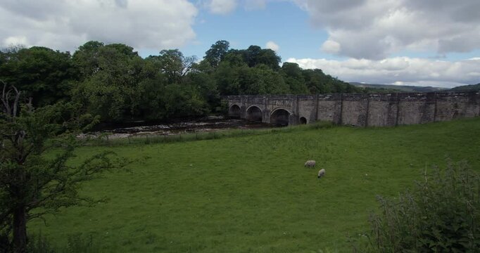 Wide shot of grassington bridge with sheep in the field in the Yorkshire Dales
