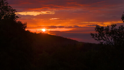 LENS FLARE, SILHOUETTE: Setting sun and sky in vibrant shades over forested hills. Breathtaking...