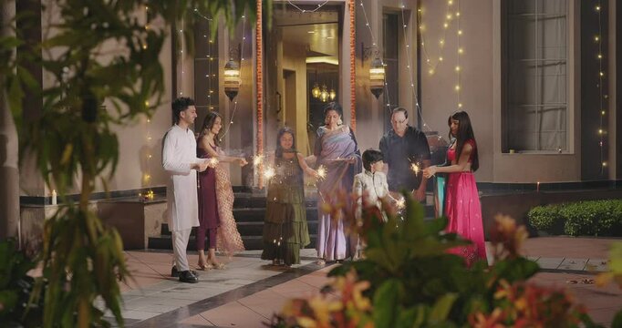 Indian Hindu Asian happy family teen girl boy child hold play crackers make fun joy night decor light diya home young adult male man female wife lady multi group older elder mom dad enjoy Diwali house