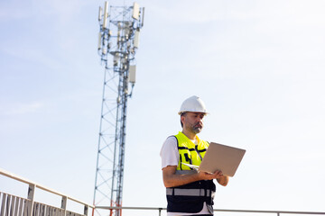 communication pole. Communications engineer checking internet signal on laptop computer at...