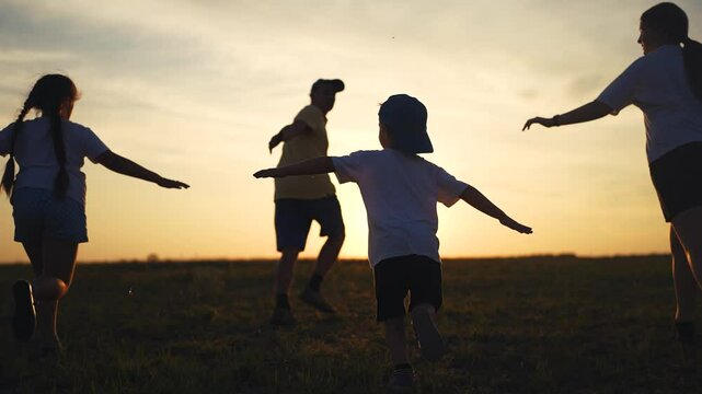 Silhouette of a family running in the park. Happy sunset meadow concept. Silhouette of children running in nature. Silhouette of a family running through nature in a park lifestyle.