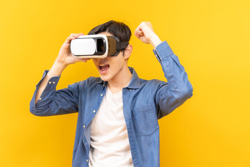 Fototapeta premium Asian young man in jacket jean and playing video games using vr with headphones on yellow background isolated.