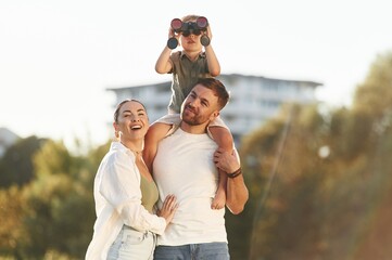 Looking far away with binocular. Mother and father are with son outdoors on the field