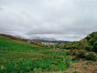 A scenic view of rolling green hills under cloudy skies near a coastal village in springtime